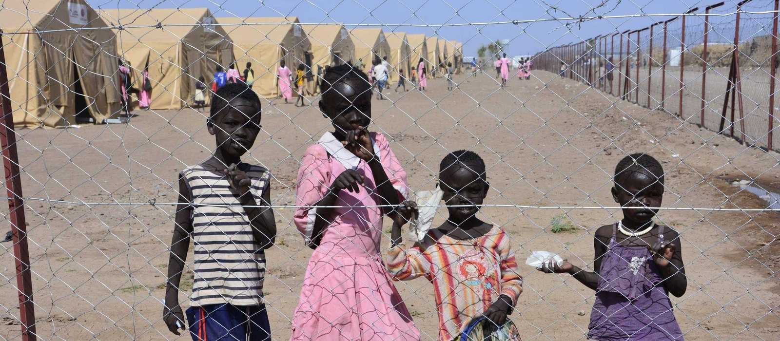 Kinder hinter einem Drahtzaun vor einem Flüchtlingslager