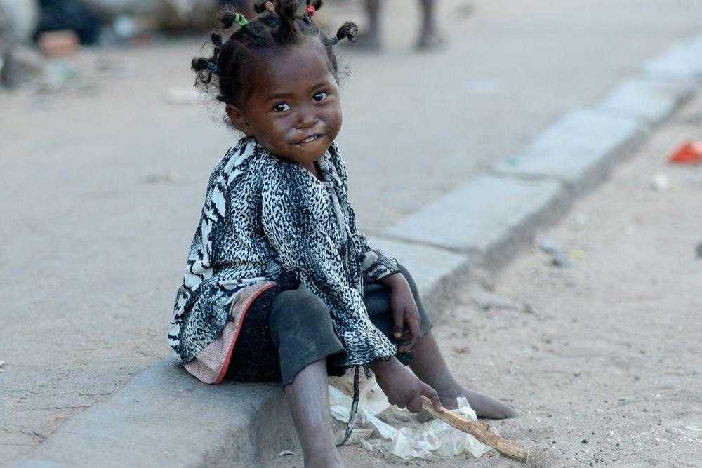 Ein kleines Mädchen, das am Straßenrand im Staub spielt