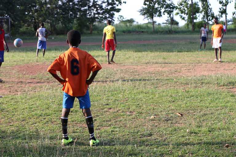 Kind in Trikot steht am Rande eines Fußballfelds