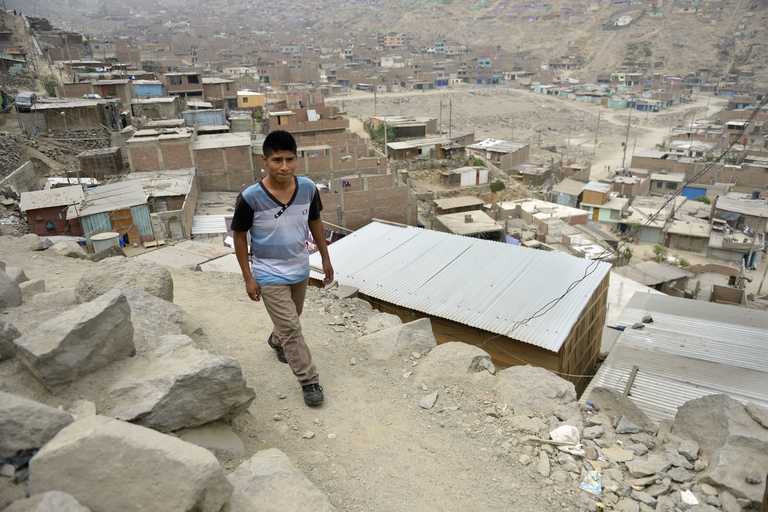 Ein Junge geht auf einem Berg hoch. Im Hintergrund sind Blechhütten des Slums zu sehen.