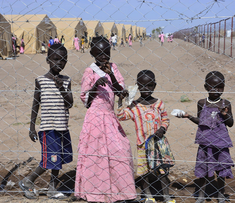 Kinder hinter einem Drahtzaun vor einem Flüchtlingslager