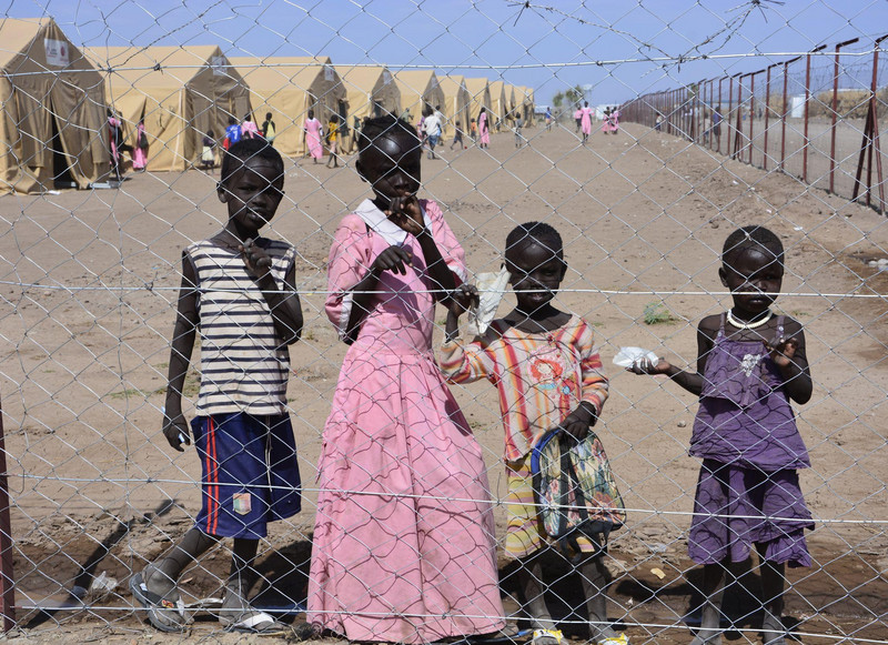 Kinder hinter einem Drahtzaun vor einem Flüchtlingslager