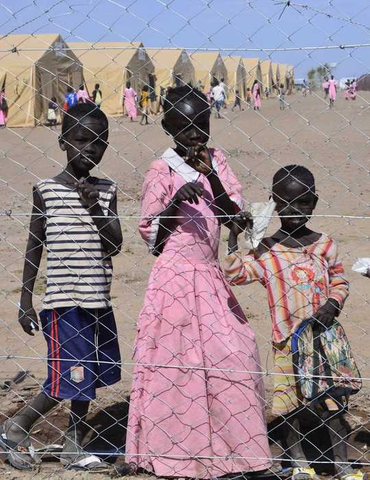 Kinder hinter einem Drahtzaun vor einem Flüchtlingslager