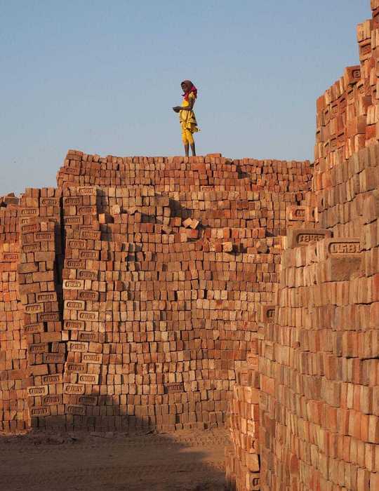 Kind steht auf einer Mauer aus Ziegeln in einer Ziegelfabrik