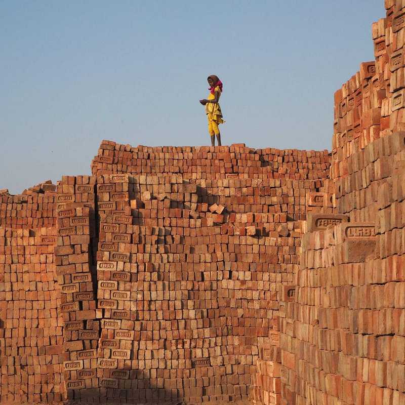 Kind steht auf einer Mauer aus Ziegeln in einer Ziegelfabrik
