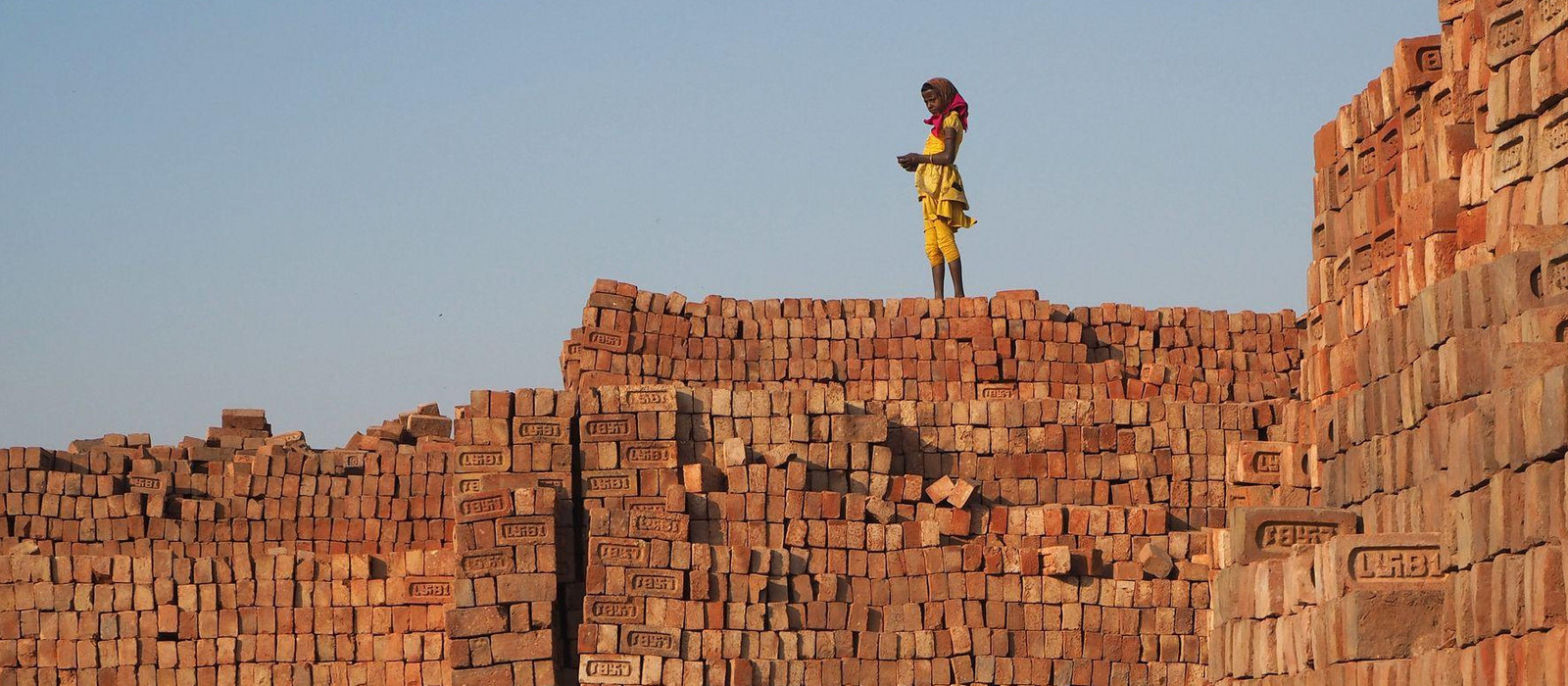 Kind steht auf einer Mauer aus Ziegeln in einer Ziegelfabrik