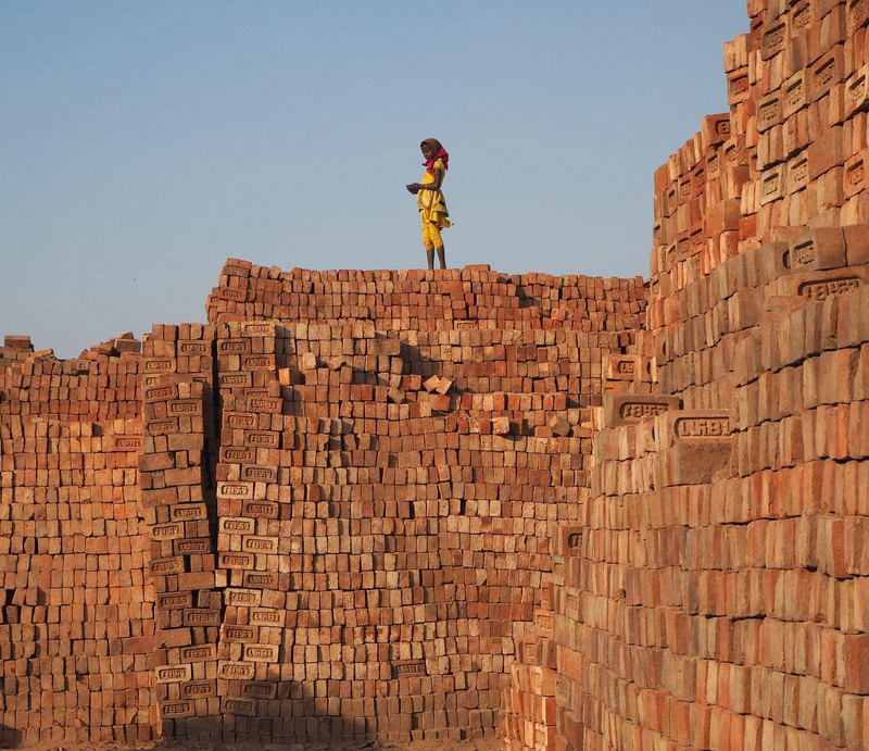 Kind steht auf einer Mauer aus Ziegeln in einer Ziegelfabrik