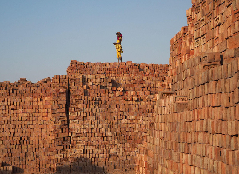 Kind steht auf einer Mauer aus Ziegeln in einer Ziegelfabrik