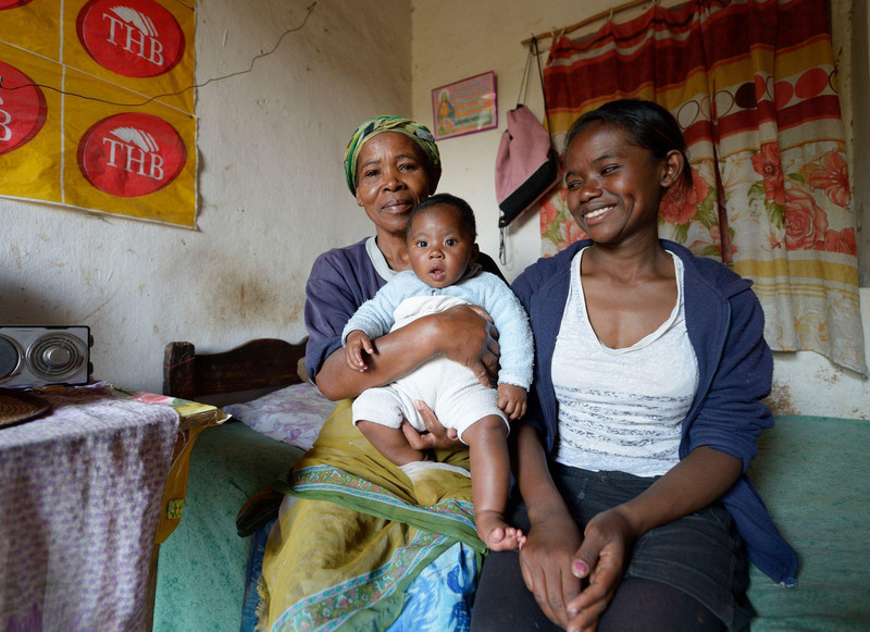 Elisa sitzt gemeinsam mit ihrer Mutter und ihrem Sohn auf einer Bettkante