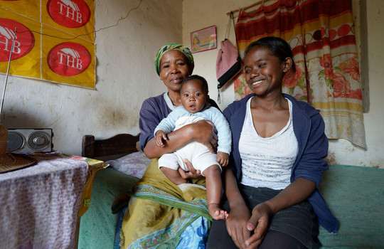 Elisa sitzt gemeinsam mit ihrer Mutter und ihrem Sohn auf einer Bettkante