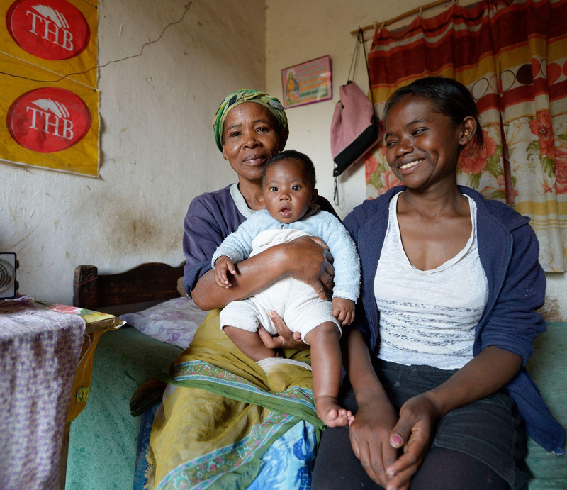 Elisa sitzt gemeinsam mit ihrer Mutter und ihrem Sohn auf einer Bettkante