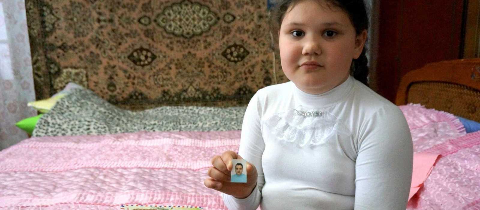 Ana sitzt auf ihrem Bett und hält ein Bild ihrer Mutter in der Hand