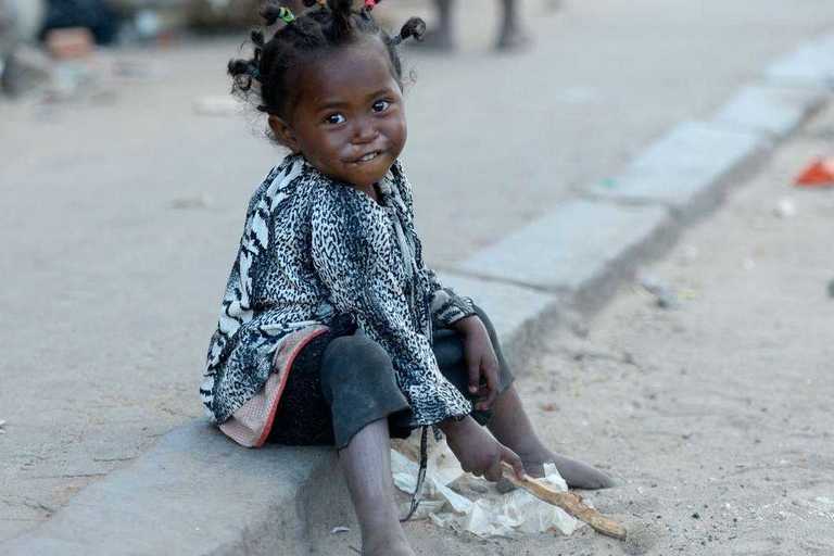 Ein kleines Mädchen, das am Straßenrand im Staub spielt