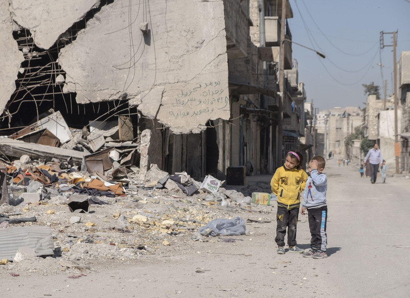 Ein kleiner Junge und ein Mädchen stehen vor den Trümmern von Aleppo