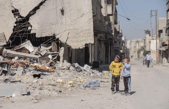 Ein kleiner Junge und ein Mädchen stehen vor den Trümmern von Aleppo