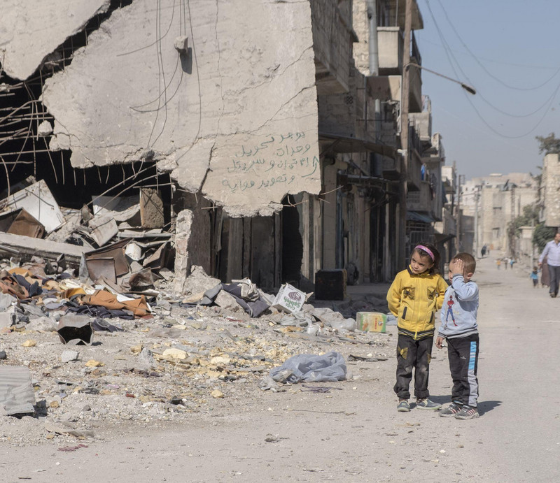 Ein kleiner Junge und ein Mädchen stehen vor den Trümmern von Aleppo