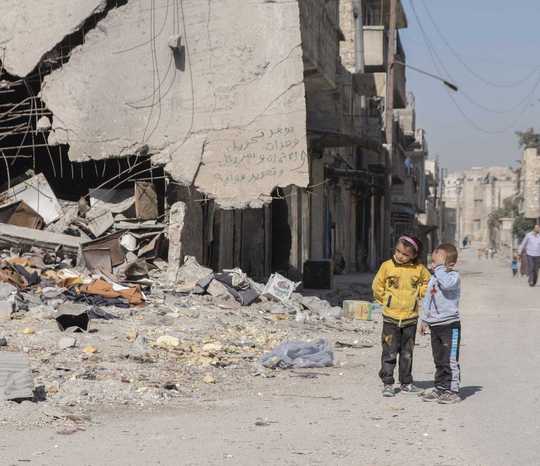 Ein kleiner Junge und ein Mädchen stehen vor den Trümmern von Aleppo