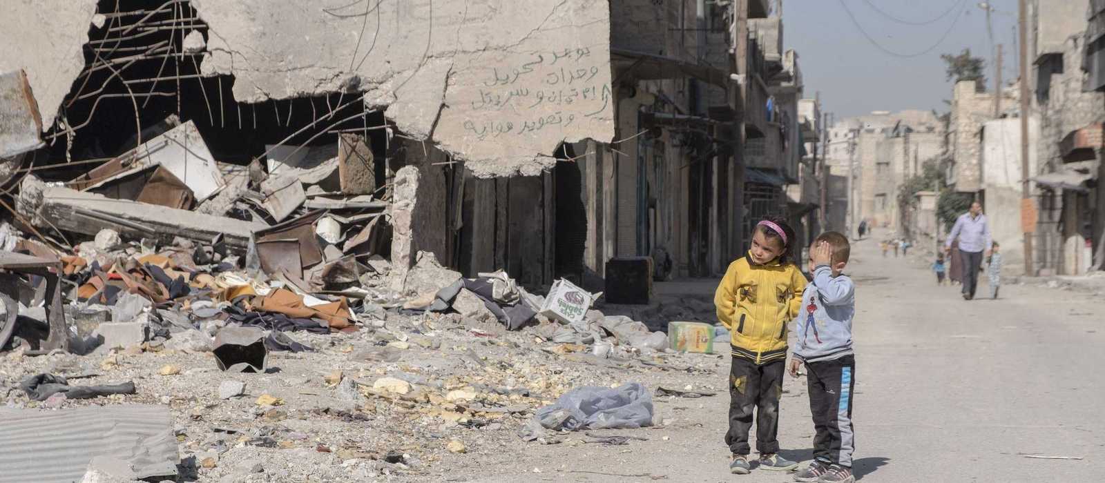 Ein kleiner Junge und ein Mädchen stehen vor den Trümmern von Aleppo
