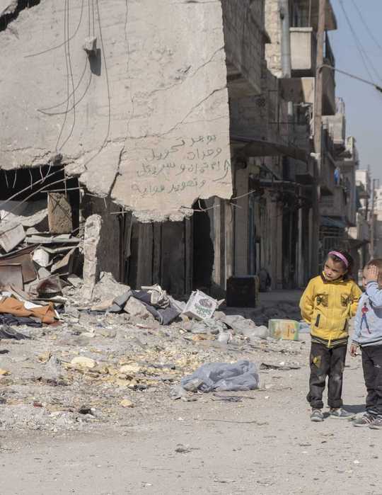 Ein kleiner Junge und ein Mädchen stehen vor den Trümmern von Aleppo