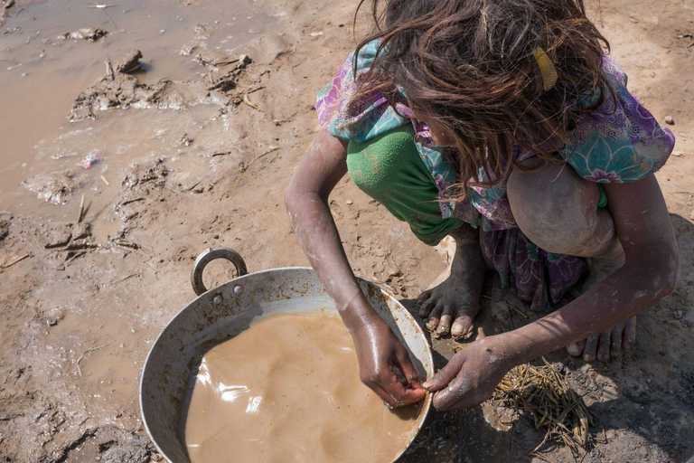 Mädchen hockt vor einem Eimer mit Wasser und Lehm