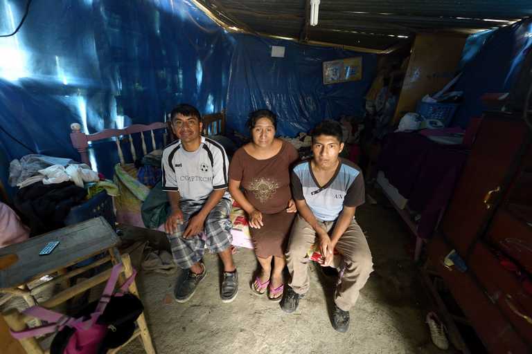 Ein Mann, eine Frau und ein Junge sitzen auf einer Liege im Innern einer Blechhütte.