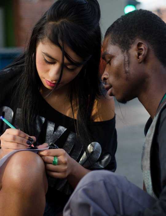 Mädchen hockt auf der Straße und schreibt einem Jungen etwas ins Schulheft