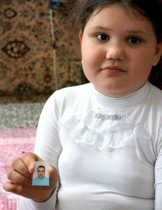 Ana sitzt auf ihrem Bett und hält ein Passfoto ihrer Mutter in der Hand